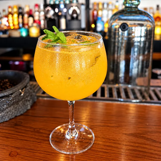 Cóctel dorado con hielo y menta servido en una copa sobre la barra
