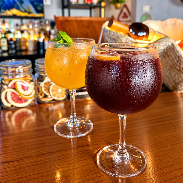 Dos cócteles en copas, uno rojo y otro dorado, sobre la barra de madera