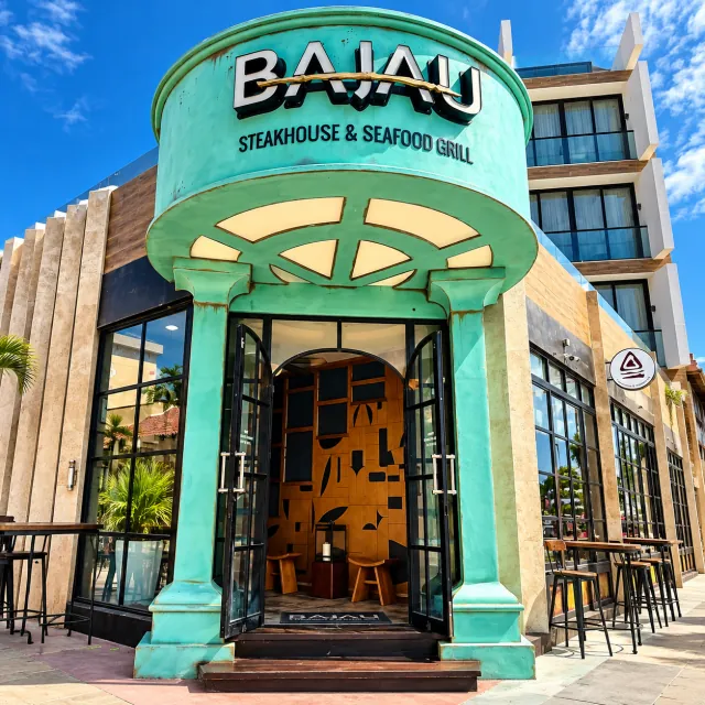 Entrada turquesa de BAJAU con el nombre del restaurante sobre las puertas abiertas